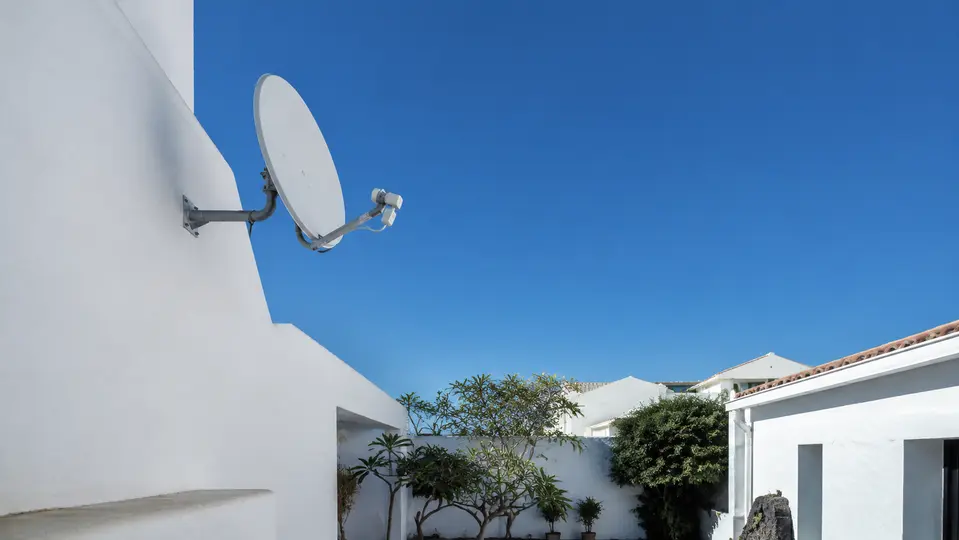 Antena satelital instalada en alto sobre una pared con cielo abierto
